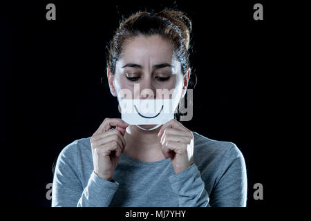 Triste et déprimé jeune belle femme latine couvrant son visage triste avec un papier découpé heureux face dans une dépression concept sur noir isolé backgrou Banque D'Images