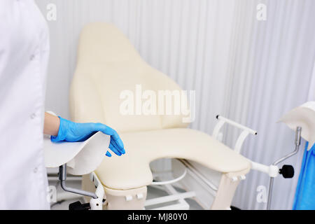La main du médecin dans un gant d'hygiène en caoutchouc sur une chaise gynécologique. Consultation des femmes Banque D'Images