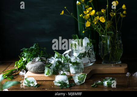 Des cubes de glace avec des fruits congelés herbes pour l'eau infusée sur fond de bois rustique Banque D'Images