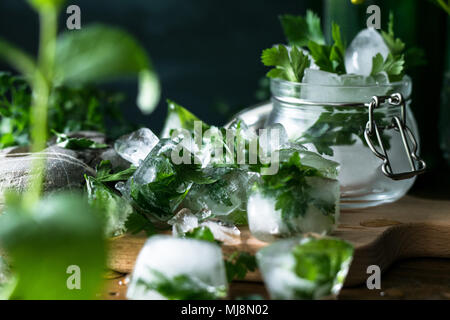 Des cubes de glace avec des fruits congelés herbes pour l'eau infusée sur fond de bois rustique Banque D'Images