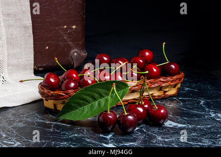 Vue rapprochée de plusieurs cerises douces rouge et grande feuille verte d'cherry tree sur la table de marbre et mûrs de cerise douce en bois jaune panier sur b Banque D'Images