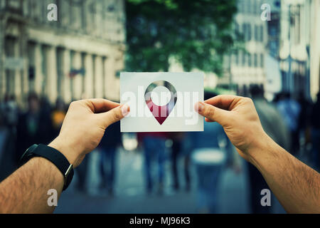Close up of man mains tenant une feuille de papier blanc avec un pointeur à l'intérieur. Le GPS à la recherche de quelqu'un sur une rue de ville bondé. Une navigation voyage Banque D'Images
