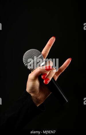 Main Femme avec red nails holding microphone avec cornes de diable rock metal sign isolé sur fond noir Banque D'Images