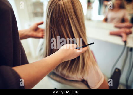 Femme blonde assise dans une chaise de salon ayant son style de cheveux au cours d'un rendez-vous avec sa coiffure Banque D'Images
