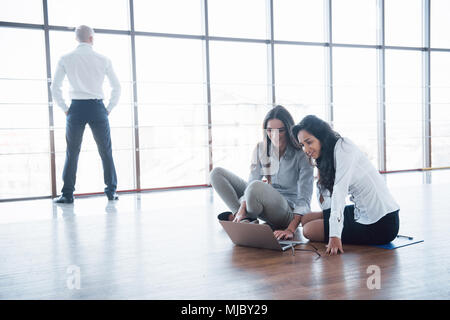 Les jeunes gens créatifs dans un bureau moderne. Groupe de jeunes gens d'affaires travaillent de concert avec l'ordinateur portable. Les pigistes assis sur le plancher. La coopération Banque D'Images