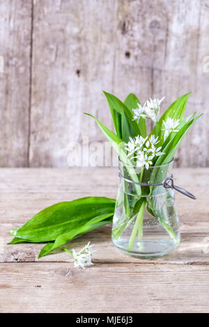 Printemps nature morte, l'ail des feuilles et fleurs d'ail sauvage dans un vase en verre sur une vieille table en bois en face d'un vieux mur en bois Banque D'Images