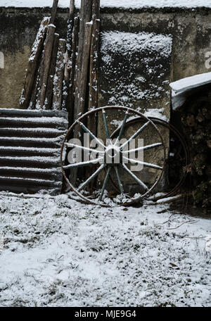 Ancienne ferme, la roue, de la tôle ondulée et de bois sur un mur, la neige Banque D'Images