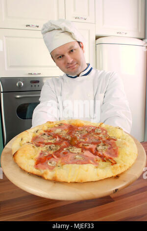 Pizza Pizza chef holding sur plaque de bois et vous regarde Banque D'Images