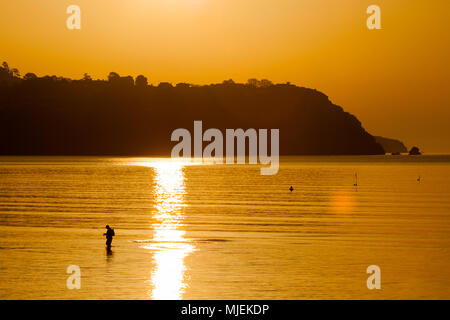 Un homme pêche dans la mer peu profonde, au large de la plage de Torquay, Devon, UK, au lever du soleil Banque D'Images