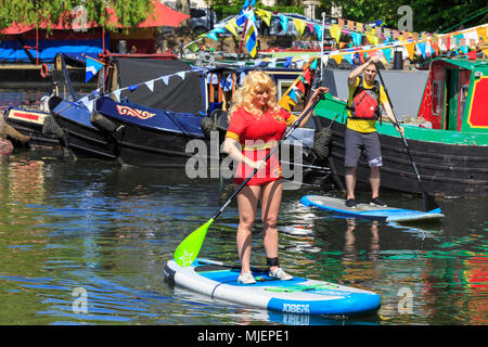 La petite Venise, Londres, 5 mai 2018. Une jeune femme habillée comme Pamela Anderson de 'Baywatch' tente paddleboarding. Les gens profiter de la Journée ensoleillée comme pleines de narrowboats remplir la Petite Venise 'pool', un bassin sur le Grand Union canal dans la petite Venise de l'eau IWA Canalway Cavalcade festival, qui célèbre la plaisance sur le British Waterways.Plus de 50 bateaux prenant part à un pagent et la concurrence, et bien d'autres qui tapissent le bord du canal pour le festival de mai 24-26th. Credit : Imageplotter News et Sports/Alamy Live News Banque D'Images