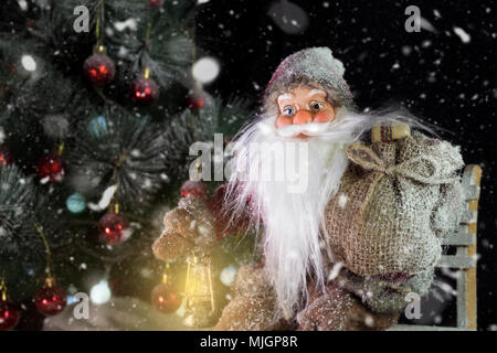 Le Père Noël en plein air à côté d'arbre de Noël dans la neige transportant des cadeaux aux enfants. Joyeux Noël & Nouvel An concept Banque D'Images