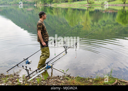 Aventures de pêche, pêche à la carpe. Pêcheur avec des cuissardes en caoutchouc vert pour la pêche et la chemise de camouflage Banque D'Images