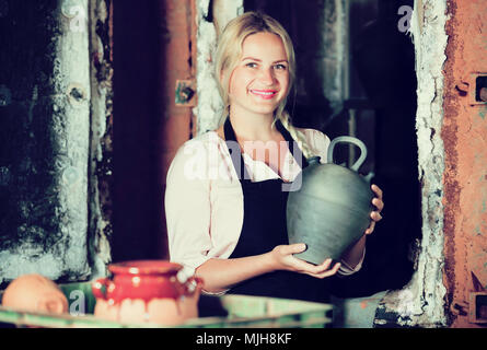 Portrait of smiling young woman holding potter en céramique émaillée noire à côté du navire Four Banque D'Images