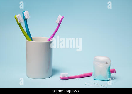 L'équipement dentaire. Brosses à dents colorées dans la tasse et du fil dentaire sur fond bleu clair. L'espace de copie, studio shot. Banque D'Images