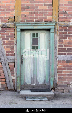 Ancienne porte en bois vert, dérésonnée, dans une maison à colombages avec briques rouges Banque D'Images