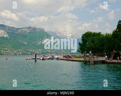 Les gens dans des bateaux à aube alors que les piétons se rassemblent le long des rives ofLake avec Annecy, enneigés des Alpes en arrière-plan, Annecy, France Banque D'Images