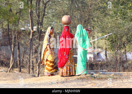 DAHMI KALAN - l'Inde, le 13 janvier 2018 : trois jeunes femmes en sari colorés rajasthani discuter près d'un bien de l'eau tout en remplissant les pots avec de l'eau Banque D'Images