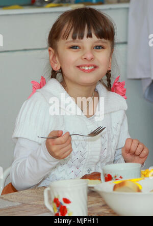 Portrait d'une belle petite fille. Elle mange le petit-déjeuner dans le jardin d'enfants et sourit à la caméra. Banque D'Images