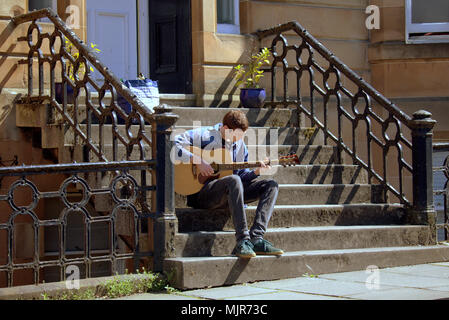 Glasgow, Écosse, Royaume-Uni le 6 mai. Météo France : jeune homme joue de la guitare sur les marches d'un immeuble de l'été ensoleillé atteint enfin la ville pour le week-end férié. Les habitants et les touristes de profiter du soleil dans le parc Kelvingrove peluche dans le West end de la ville. Gérard Ferry/Alamy news Banque D'Images