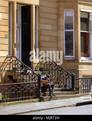 Glasgow, Écosse, Royaume-Uni le 6 mai. Météo France : jeune homme joue de la guitare sur les marches d'un immeuble de l'été ensoleillé atteint enfin la ville pour le week-end férié. Les habitants et les touristes de profiter du soleil dans le parc Kelvingrove peluche dans le West end de la ville. Gérard Ferry/Alamy news Banque D'Images