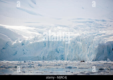 Zodiac avec les passagers explore les eaux au-dessous de la falaise de glace massive - l'avant-garde de l'un des glaciers de l'Antarctique. Banque D'Images