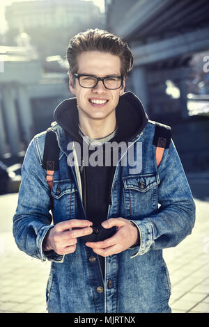 L'homme souriant avec des lunettes en choisissant l'établissement City avec un sac à dos Banque D'Images