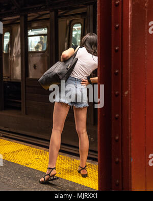 New York, États-Unis, 5 mai 2018. Une femme se penche sur le bord de la plate-forme pour vérifier l'arrivée d'un train dans une station de métro de la ville de New York. Photo Banque D'Images