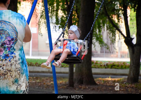 Krasnodar, Russie - Août 28, 2017 : Petite fille se balançant sur une balancelle sous la surveillance d'adultes dans le parc. Banque D'Images