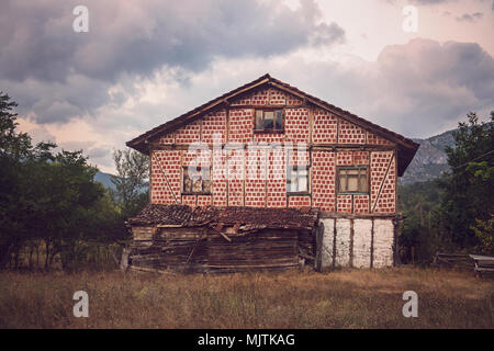 Une maison rustique abandonnée dans un cadre rural avec une façade à damiers rouge et blanc, de vieilles poutres en bois et un toit en décomposition, Banque D'Images