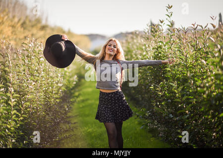 Portrait de jeune femme blonde heureux à bras ouverts en chemin rural. Girl wearing swater, jupe et chapeau Banque D'Images