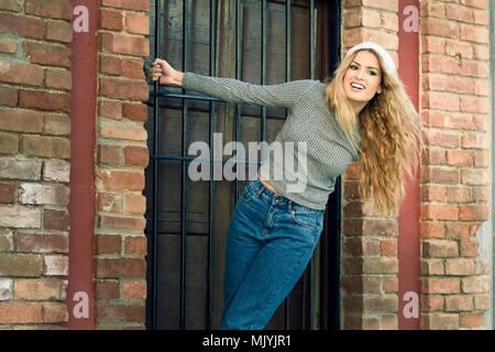 Jeune femme portant des vêtements décontractés smiling en contexte urbain. Girl wearing sweater et blue-jeans Banque D'Images