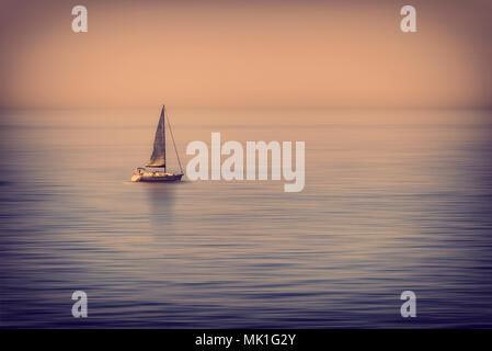 Lonely voilier au milieu de la mer calme au coucher du soleil Banque D'Images