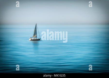 Lonely voilier au milieu de la mer calme au coucher du soleil Banque D'Images