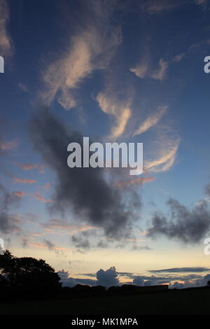 Beau Lever de soleil nuages sur un ensemble sombre des arbres menant à un magnifique ciel bleu avec des nuages pastel éclairées par le soleil du matin Banque D'Images