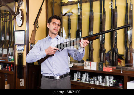 Cheerful male hunter choisissant fusil en magasin avec l'équipement de recherche de Banque D'Images