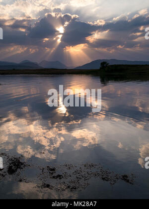 Rayons de soleil rayonnant à travers les nuages et se reflètent dans les eaux de la baie de Broadford toujours avec du rouge au-delà de montagnes Cuillin, Isle of Skye, Scotland, UK Banque D'Images