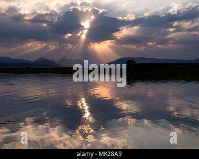 Rayons de soleil rayonnant à travers les nuages et se reflètent dans les eaux de la baie de Broadford toujours avec du rouge au-delà de montagnes Cuillin, Isle of Skye, Scotland, UK Banque D'Images