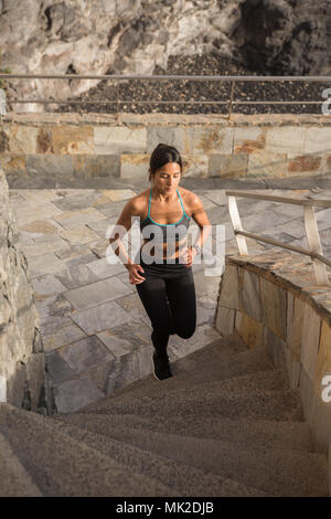 Mettre en place une jeune femme s'exécute jusqu'à l'escalier gris soleil sur sa peau et le port de collants noirs et un tank top Banque D'Images