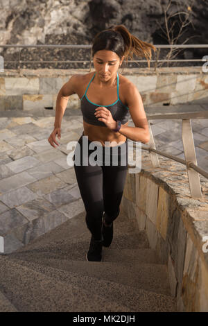 Une jeune femme sportive concentrée sur la course en haut de l'escalier en collants et top avec ses cheveux attachés en arrière Banque D'Images