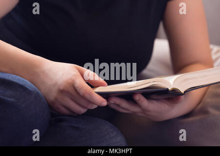 Jeune femme de détente sur le canapé de la lecture de la Bible Banque D'Images