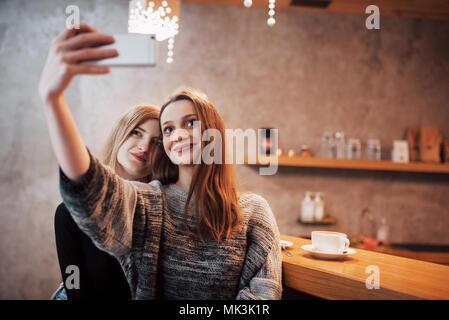 Deux amis de boire du café dans un café, en tenant vos autoportraits avec un téléphone intelligent et s'amuser faire des grimaces. Se concentrer sur la fille sur la gauche Banque D'Images