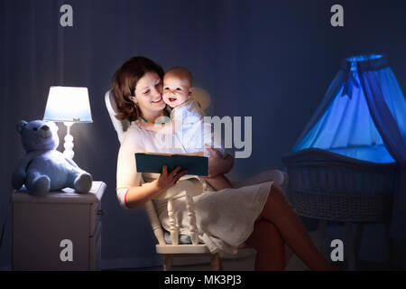 La mère et l'enfant de lire un livre dans une chambre sombre. Maman et enfant à lire les livres avant de le mettre au lit. Famille dans la soirée. Chambre d'enfant intérieur avec une lampe de nuit Banque D'Images