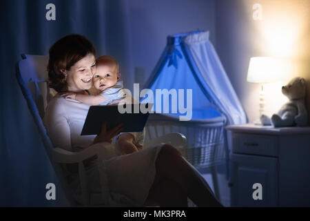 La mère et l'enfant de lire un livre dans une chambre sombre. Maman et enfant à lire les livres avant de le mettre au lit. Famille dans la soirée. Chambre d'enfant intérieur avec une lampe de nuit Banque D'Images