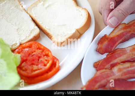 Un homme s'apprête à mettre sur pied un bacon, laitue et tomate sandwich sur pain blanc. Banque D'Images