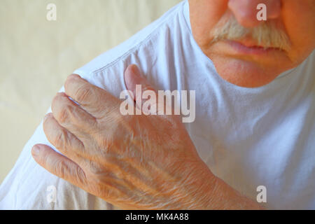 Man un t-shirt blanc avec sa main sur une épaule douloureuse Banque D'Images