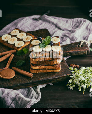 Toasts à la française carré de pain blanc avec du chocolat et des morceaux de banane sur une planche en bois, vintage toning Banque D'Images