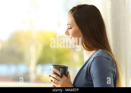 Vue latérale du portrait d'une dame pensive tenant une tasse de café à côté d'une fenêtre Banque D'Images