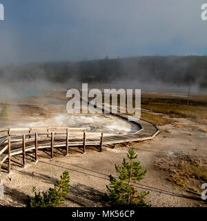 Passerelle en bois qui traverse l'énergie géothermique piscines d'eau chaude avec de la vapeur s'élevant du sol sous un ciel bleu rempli de nuages de vapeur. Banque D'Images