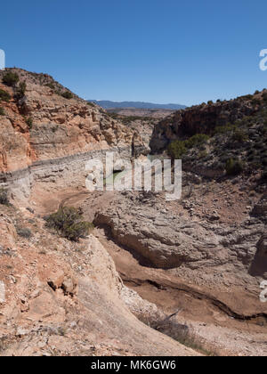 Les parois du canyon coloré de Bighorn Canyon National Recreation Area avec végétation en premier plan avec de minces nuages et ciel bleu au-dessus. Un terrain boueux t Banque D'Images