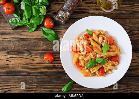 Pâtes penne à la sauce tomate avec du poulet, tomates, décoré avec du basilic sur une table en bois. Cuisine italienne. Les pâtes à la bolognaise. Vue d'en haut Banque D'Images